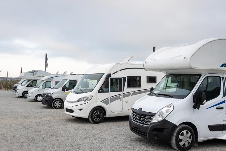 Grupp vita husbilar parkerade på parkeringen på en camping.